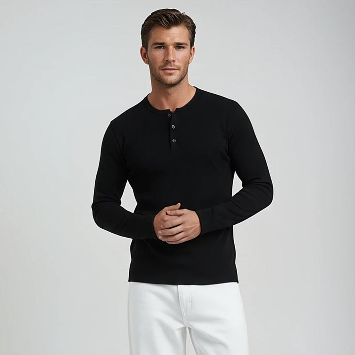 Man wearing a black long-sleeve henley shirt and white pants on a light gray background